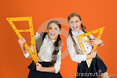 School students learning geometry. Kids school uniform on orange background. Pupil cute girls with big rulers. Geometry Stock Photo