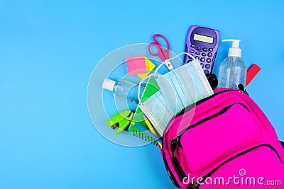 Backpack full of school supplies and COVID 19 prevention items. Top view, spilling onto a blue background. Back to school during p Stock Photo