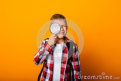 Schoolboy boy looking through a magnifying glass, enlarging his eye on a yellow background Stock Photo