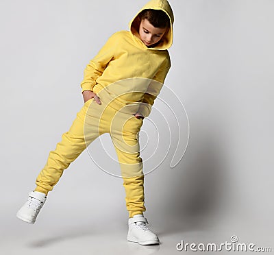Schoolboy in bright yellow sportswear and white sneakers on a white background. The tough guy in the hood stuck his Stock Photo