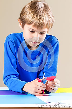 Schoolboy cutting colored paper with scissors at the table Stock Photo