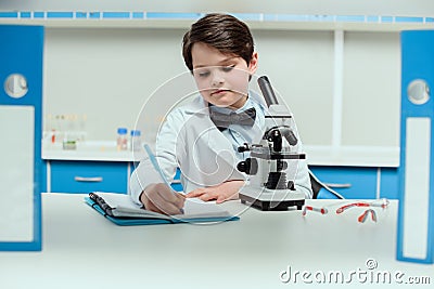 Schoolboy with microscope and copybook in science laboratory Stock Photo