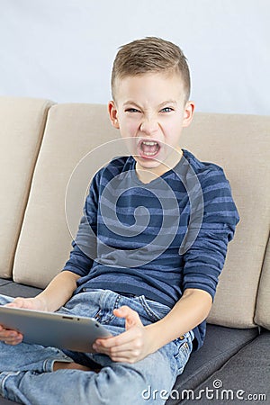 A schoolboy plays a videogame on tablet computer, showing anger and agression Stock Photo