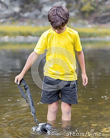 A schoolboy stands in the river on outdooor and destroys a mirrorless photo camera Stock Photo