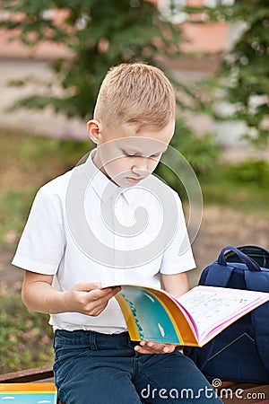 Schoolboy in uniform sitting on a bench and reading schoolbook Stock Photo