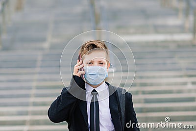 Schoolboy walks out of school wearing protective mask in a city Stock Photo
