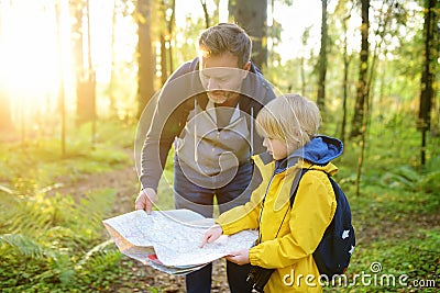 Schoolchild and his mature father hiking together and exploring nature. Little boy with dad looking map during orienteering in Stock Photo