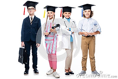 schoolchildren in costumes of different professions and graduation caps looking at camera Stock Photo