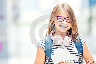 Schoolgirl with bag, backpack. Portrait of modern happy teen school girl with bag backpack headphones and tablet. Stock Photo