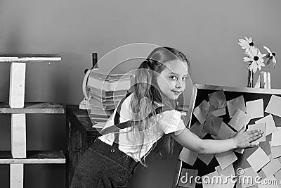 . Schoolgirl with cunning face in her classroom. Girl with ponytails puts sticky notes on blackboard near flowers Stock Photo