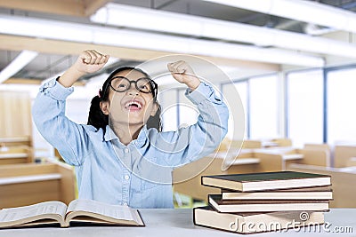 Schoolgirl lifting hands with books in classroom Stock Photo