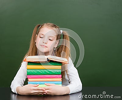 Schoolgirl with pile books near empty green chalkboard Stock Photo