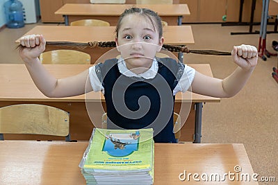 A schoolgirl in a school uniform holds pigtails with her hands and looks in surprise at the camera. Fatigue and Editorial Stock Photo