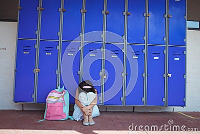 Schoolgirl sitting on pavement by lockers in corridor Editorial Stock Photo