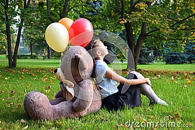 Sad baby girl with big teddy bear and balloons in the park. Problems teenagers at school Stock Photo