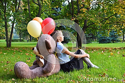 Sad girl with big teddy bear and balloons in the park. Problems teenagers at school Stock Photo