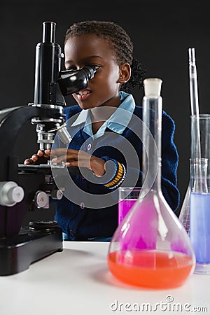 Schoolgirl using microscope against black background Stock Photo