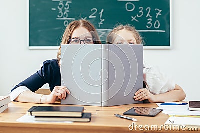 Schoolgirls hiding behind book sitting in a classroom Stock Photo