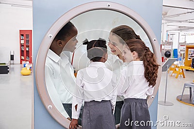 Schoolgirls looking in a magnifying mirror at science centre Stock Photo