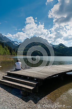 Schwarzsee, FR / Switzerland - 1 June 2019: woman tourist and pet dog enjoy the summer lakeside view at the Schwarzsee Lake in the Editorial Stock Photo