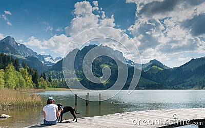 Schwarzsee, FR / Switzerland - 1 June 2019: woman tourist and pet dog enjoy the summer lakeside view at the Schwarzsee Lake in the Editorial Stock Photo