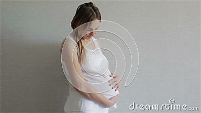 Schönes junges schwangeres Mädchen mit einem Zopf im Studio auf einem grauen Hintergrund stock video Schönes junges schwangeres Mädchen mit einem Zopf im Studio auf einem grauen Hintergrund stock video