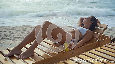 Schönheit im weißen Badeanzug und in den Sonnenbrillen liegt auf einem hölzernen Sonnenruhesessel auf dem Seestrand stock video Schönheit im weißen Badeanzug und in den Sonnenbrillen liegt auf einem hölzernen Sonnenruhesessel auf dem Seestrand stock video