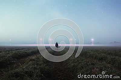 A science fiction concept. A man standing in a field back to camera looking into the sky, with glowing UFO orbs on the horizon Stock Photo