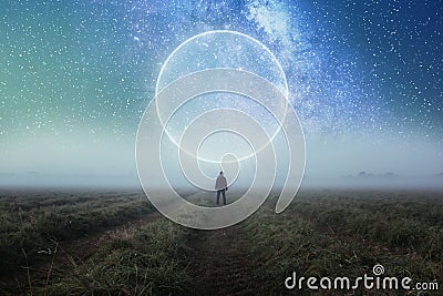 A science fiction concept. A man standing in a field looking out across space with a glowing portal in the night sky Stock Photo