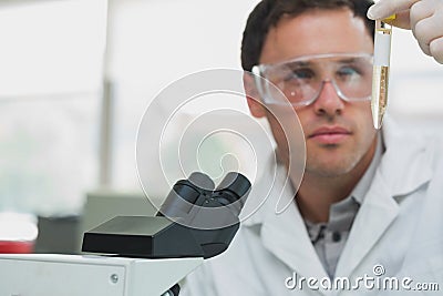 Scientific researcher looking at test tube while using microscope in lab Stock Photo