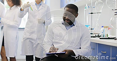 Scientifique féminin Discuss Test Tube avec le collègue d'Afro-américain tandis que chercheurs Team Making Experiment In Lab clips vidéos Scientifique féminin Discuss Test Tube avec le collègue d'Afro-américain tandis que chercheurs Team Making Experiment In Lab clips vidéos