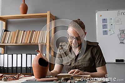 Scientist archaeologist working in office reading book studying ancient vase from textbook Stock Photo