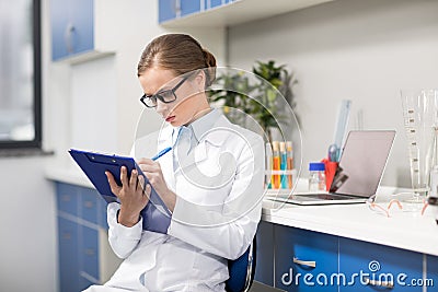 Scientist in eyeglasses writing in clipboard in research laboratory Stock Photo