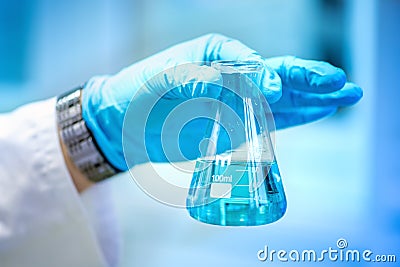 Scientist hand holding glass with blue liquid, making experiments and carrying out probes Stock Photo