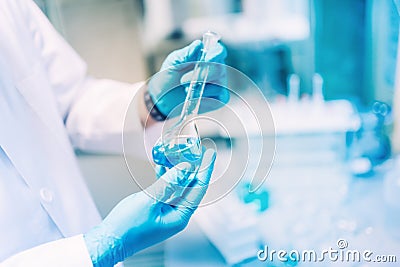 Scientist holding glass with blue liquid, conducting experiments and carrying out probes in special laboratory Stock Photo