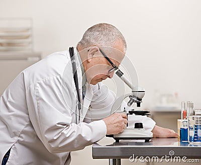 Scientist in lab coat peering through microscope Stock Photo