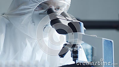 Scientist in protection suit and masks working in research lab using laboratory equipment: microscopes, test tubes Stock Photo