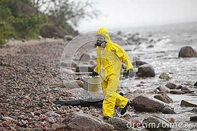 Scientist in protective suit with silver case walking in on rocky beach Stock Photo