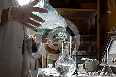 Scientist in a white coat and gloves conducts an experiment, he pours liquid from one flask to another, in the Stock Photo