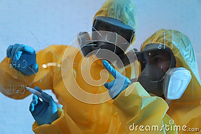 Scientists in chemical protective suits writing formula on glass board. Virus research Stock Photo