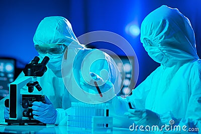 Scientists in protection suits and masks working in research lab using laboratory equipment: microscopes, test tubes Stock Photo