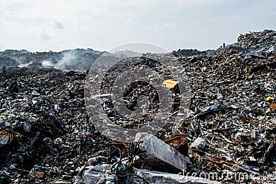 Scrap heap at the garbage dump full of smoke, litter, plastic bottles,rubbish and trash at tropical island Stock Photo