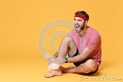 Screaming bearded fitness sporty guy sportsman in headband t-shirt in home gym isolated on yellow background. Workout Stock Photo