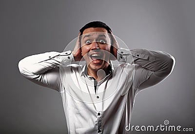 Screaming shocked young business man looking with wide open mouth and holding the hands the head on grey background. Closeup Stock Photo