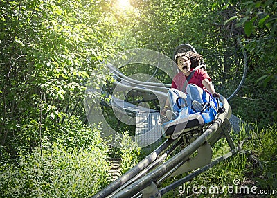 Screaming teen girl riding downhill on an outdoor roller coaster on a warm summer day. Stock Photo