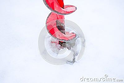 of ice drill, painted with red paint, it cuts into ice and snow in lake or river. Drilling holes in ice - winter fishing sce Stock Photo