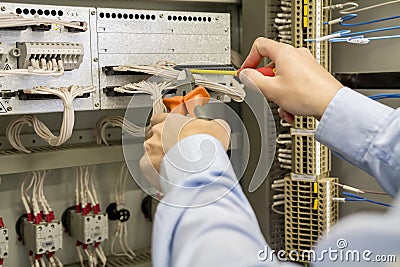 Screwdriver and wire cutters in hands of electrician against electric box with terminal, wires and controllers Stock Photo