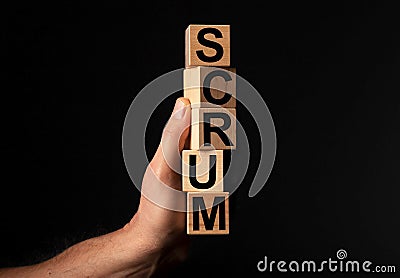 Scrum word on wood cube blocs in male hand over black background. Concept of methods in management Stock Photo