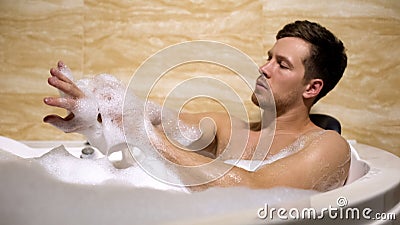 Scrupulous man soaping himself with loofah, taking bath with foam, cleanness Stock Photo