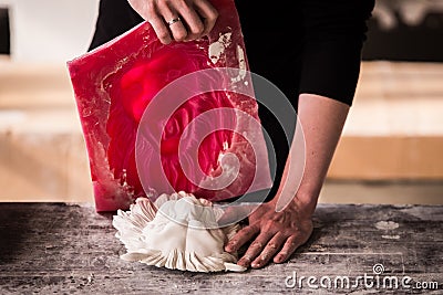 The sculptor works in a plaster workshop. Separates the silicone mold from the plaster sculpture of the lion`s head. Stock Photo